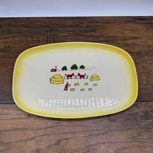 Peut inclure: Un plat de service ovale avec un centre crème et une bordure jaune. Le centre présente une illustration graphique d'une scène de ferme avec deux chevaux rouge foncé, une grange rouge, des meules de foin jaunes et une personne au travail.