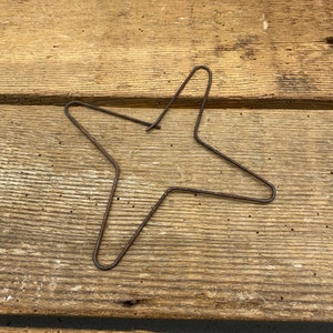 May include: A rustic, wire star-shaped ornament made of brown metal. The star is lying flat on a wooden surface.