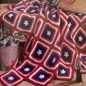 May include: A red, white, and blue crocheted blanket with a star pattern. The blanket is draped over a brick surface. A metal bucket of drinks and small flags are in the background.