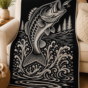 May include: A black and white woven throw blanket featuring a large graphic of a bass fish jumping out of water. The design includes a fishing lure in the fish's mouth, stylised water splashes, and a background of pine trees along the shoreline.