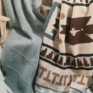 May include: Two crocheted blankets. One is light blue with a diamond pattern. The other is cream-colored with brown and blue geometric designs. The blankets are folded and draped over a surface, showcasing their textures and colors.
