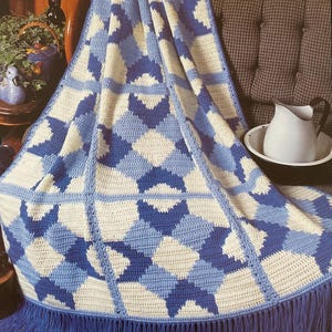 May include: A blue and white crocheted blanket with a star design. The blanket is fringed along the bottom edge and is draped over a chair. The text "Scattered Stars" is at the bottom of the image.