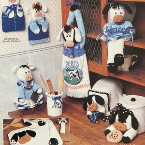 May include: A collection of crochet cow-themed kitchen accessories, including pot holders, a towel, and decorative figures. The items are primarily white, black, and blue, with some featuring the text "Welcome" and "5% Milk".