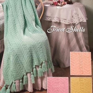 May include: A mint green crochet blanket with a chevron pattern and tassels. The blanket is draped over a chair. The image also shows a table with a lace tablecloth and a framed photo. The text "Picot Shells" is visible.