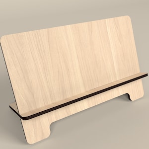 Puede incluir: Un soporte de teléfono de madera con un borde marrón oscuro. El soporte está inclinado para sostener un teléfono o una tableta en posición vertical.