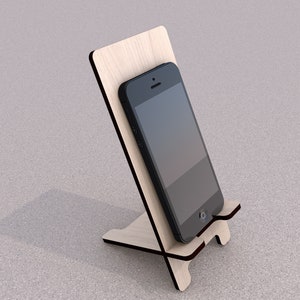 May include: A wooden phone stand with a black smartphone resting on it. The stand is made of light wood and has a simple design.