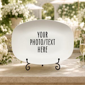 May include: A white oval ceramic platter displayed on a black metal scrollwork stand. The center of the platter features the black text "YOUR PHOTO/TEXT HERE" in a clean, sans-serif font, positioned for custom personalization.
