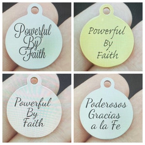 May include: Four round metal charms with different finishes. The charms have the text "Powerful By Faith" in black lettering. The fourth charm has the text "Poderosos Gracias a la Fe" in black lettering.