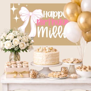 May include: A birthday celebration with a cake, cupcakes, cookies, and balloons. The backdrop features a sign that says "Happy Birthday Millie" with a bow and stars. A bouquet of white roses sits in a glass vase.