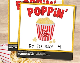 May include: A red and white striped popcorn bucket with the words "POP CORN" in a red circle. The bucket is filled with popcorn and there are three popcorn kernels on the white background. The text "POPPIN' BY TO SAY Hi!" is in red and black letters. The text "Davis Realistate Company HUNTER DAVIS +123-456-7890 www.reallygreatsite.com" is in black letters.