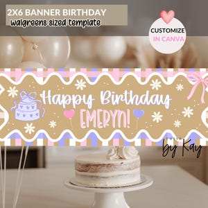 May include: A birthday banner with the text "Happy Birthday EMERYN!" in a playful font, decorated with flowers, balloons, and a cake illustration. The banner has a tan background with pink and blue checkered patterns. A cake on a white cake stand is in the foreground.