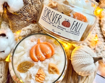 May include: Two glass jars of soy blend wax candles labeled Forever Fall. The candles are topped with wax shapes including orange pumpkins, brown leaves, and tan waffles, dusted with gold glitter. The label lists scents and a net weight of 12oz/340g.