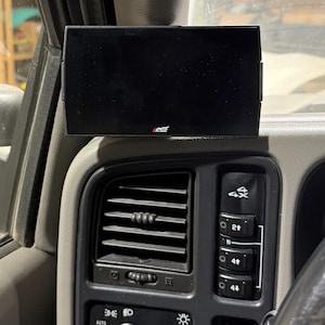 Peut inclure: Un moniteur Edge noir installé sur le tableau de bord d'un véhicule. L'écran rectangulaire est noir. Le tableau de bord gris comporte des bouches d'aération, des boutons de commande et un sélecteur 4x4. Le logo Edge est visible.
