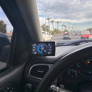 May include: A black car interior with a digital display showing a speedometer reading of 147 mph, a tachometer reading of 86, and a temperature reading of 95 degrees. The car's steering wheel is visible in the foreground.