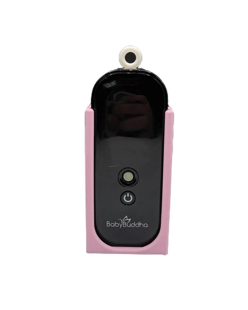 K&ouml;nnte beinhalten: Ein schwarzer und rosa Babyphone mit dem Text "Baby Buddha" auf der Vorderseite. Der Monitor hat einen schwarzen Bildschirm und einen Ein-/Ausschalter. Der Monitor ist in einem rosa Schutzgeh&auml;use untergebracht und hat eine kleine wei&szlig;e und schwarze Kamera oben.