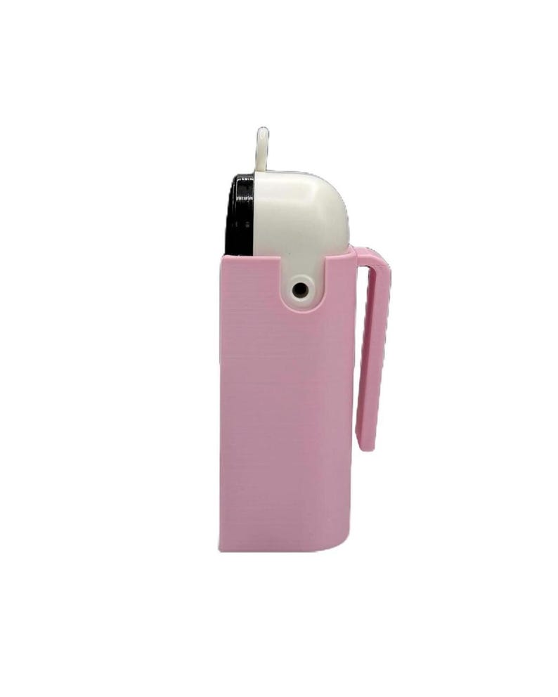 K&ouml;nnte beinhalten: Ein tragbarer Luftreiniger in Rosa und Wei&szlig; mit Griff. Der obere Teil ist wei&szlig; mit einem schwarzen Schlitz, und der untere Teil ist in einer rosa Halterung mit Griff eingeschlossen. Der Reiniger hat oben eine kleine Schlaufe.
