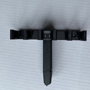 May include: A black plastic wall mount with a vertical, cylindrical holder. The mount has two horizontal arms with slots for holding objects.