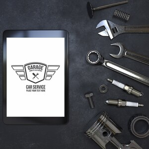 Puede incluir: Una tableta negra con una pantalla blanca que muestra un logotipo para un servicio de reparaci&oacute;n de autom&oacute;viles de garaje. El logotipo presenta un escudo con alas y el texto "Garage Complete Auto Repair Car Service Place Your Text Here". La tableta est&aacute; rodeada de varias piezas y herramientas de autom&oacute;viles, incluidas llaves, buj&iacute;as y un pist&oacute;n.