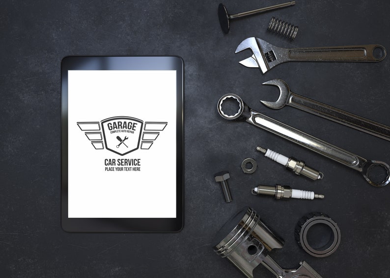 Puede incluir: Una tableta negra con una pantalla blanca que muestra un logotipo para un servicio de reparaci&oacute;n de autom&oacute;viles de garaje. El logotipo presenta un escudo con alas y el texto "Garage Complete Auto Repair Car Service Place Your Text Here". La tableta est&aacute; rodeada de varias piezas y herramientas de autom&oacute;viles, incluidas llaves, buj&iacute;as y un pist&oacute;n.