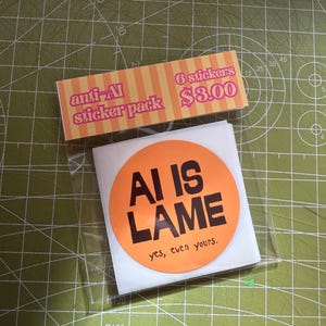 May include: A pack of circular stickers in a clear plastic sleeve. The top label features orange and yellow stripes with the text anti-AI sticker pack and 6 stickers. The main sticker is orange with the black text AI IS LAME and yes, even yours.