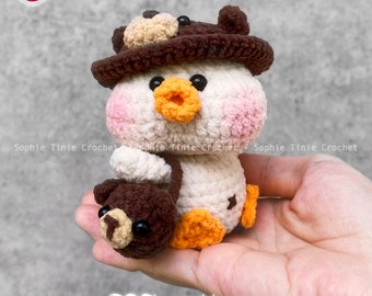 May include: Crochet pattern for a plush toy of a white bird wearing a brown hat with a bear face on top. The bird is holding a brown bear plush toy. The pattern is available as a PDF download.  "PDF pattern"