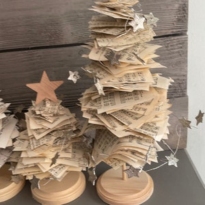 May include: Two miniature Christmas trees made of stacked sheet music with wooden bases and silver glitter stars.