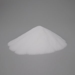 May include: A pile of fine, white powder, possibly a granular substance like sugar or salt, is centered against a plain gray background. The powder forms a small, rounded mountain shape, with soft, textured edges.