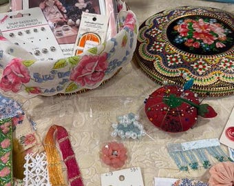 May include: A collection of craft supplies including a basket with a Dream Spinners booklet, snap fasteners, and embroidery thread. Also, a decorative round box, buttons, ribbons, and a strawberry-shaped pin cushion.