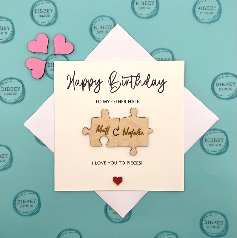 May include: A white card with a handwritten message that says "Happy Birthday to my other half."  The card has a wooden puzzle piece with the names "Matt & Natalie" on it. The card also has the text "I love you to pieces!" and a small red heart.