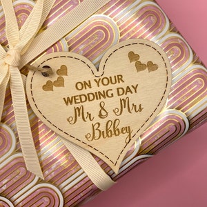 K&ouml;nnte beinhalten: Ein h&ouml;lzerner Geschenkanh&auml;nger in Herzform mit dem Text "On Your Wedding Day Mr & Mrs Bibbey" und kleinen Herzen, die in den Anh&auml;nger graviert sind.