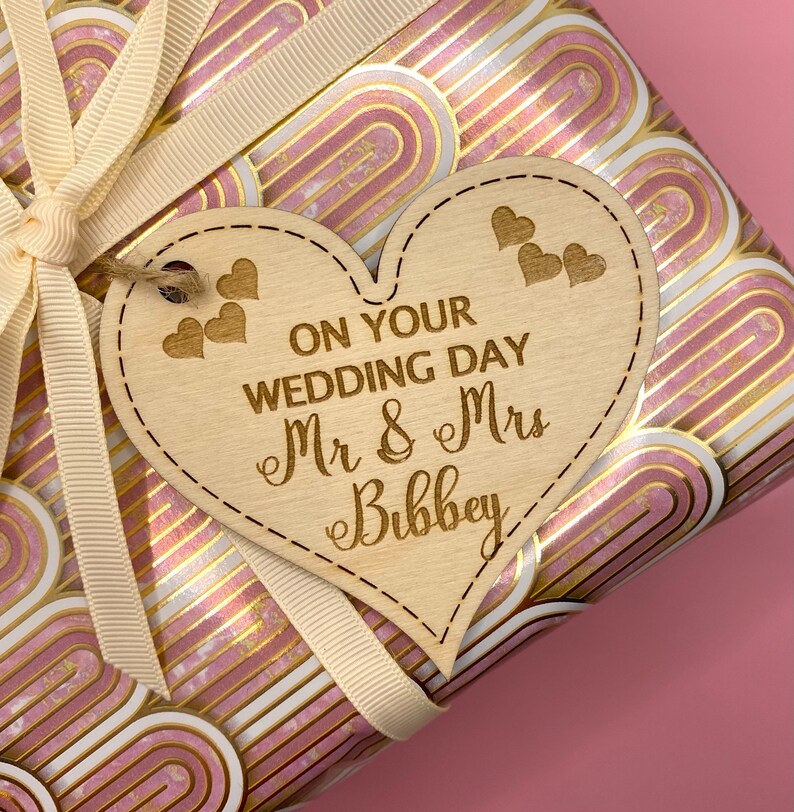 K&ouml;nnte beinhalten: Ein h&ouml;lzerner Geschenkanh&auml;nger in Herzform mit dem Text "On Your Wedding Day Mr & Mrs Bibbey" und kleinen Herzen, die in den Anh&auml;nger graviert sind.