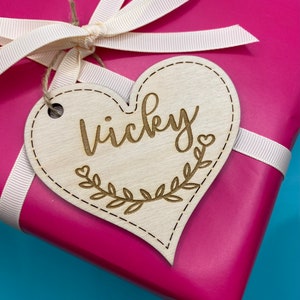 K&ouml;nnte beinhalten: Ein h&ouml;lzerner Geschenkanh&auml;nger in Herzform mit dem eingravierten Namen "Vicky". Der Anh&auml;nger ist mit einem Blattdesign und einem kleinen Herzen verziert.