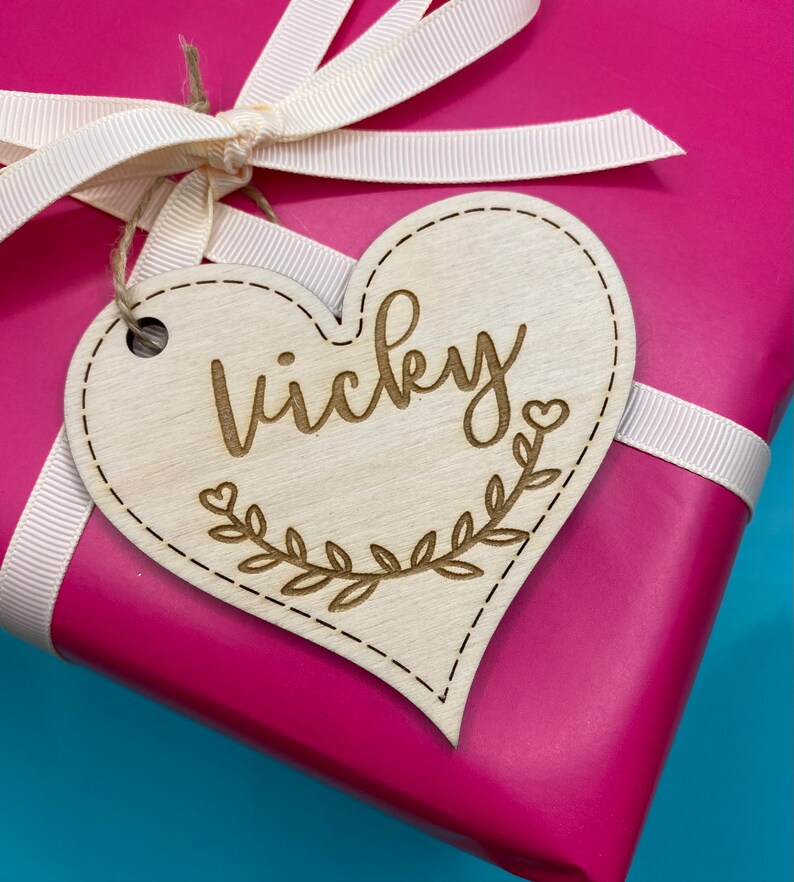 K&ouml;nnte beinhalten: Ein h&ouml;lzerner Geschenkanh&auml;nger in Herzform mit dem eingravierten Namen "Vicky". Der Anh&auml;nger ist mit einem Blattdesign und einem kleinen Herzen verziert.