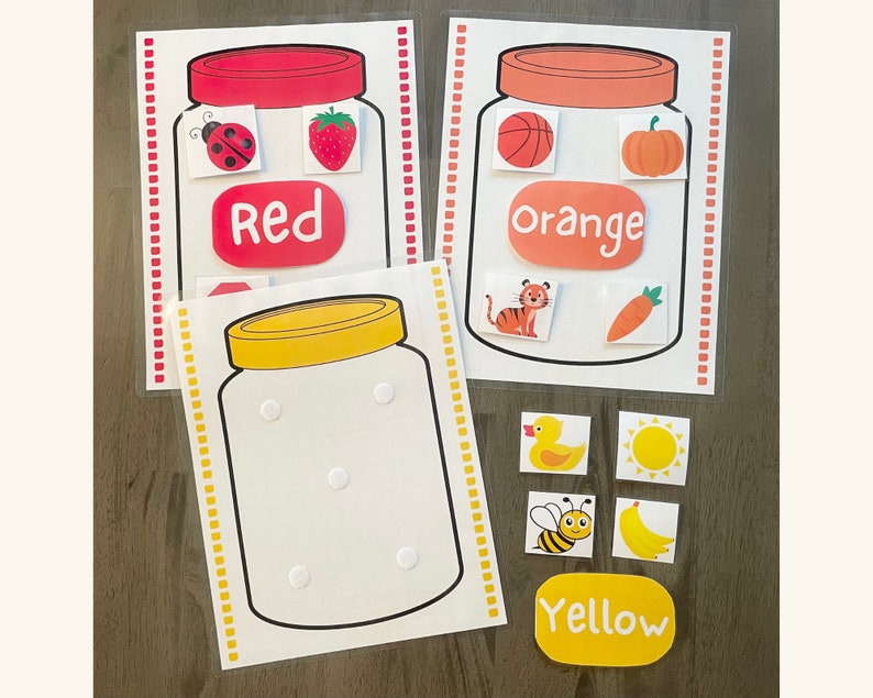 May include: Three printable jar activity cards for kids. The cards feature a red jar with a ladybug, strawberry, and the word "Red", an orange jar with a basketball, pumpkin, and the word "Orange", and a yellow jar with the word "Yellow".