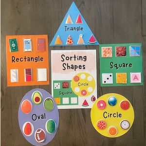 Pode incluir: Um conjunto de cartas de classificação coloridas para ensinar formas às crianças. As cartas apresentam diferentes formas, incluindo círculos, quadrados, triângulos, retângulos e ovais. Cada carta tem uma variedade de imagens que representam a forma, como uma fatia de pizza para um triângulo, uma melancia para um círculo e uma porta para um retângulo.