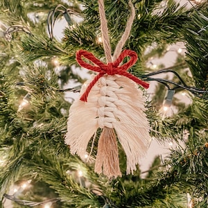 Op de afbeelding: Een witte en beige macramé-versiering met een rode strik die aan een kerstboom hangt.