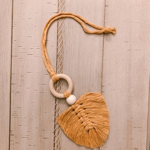 May include: A mustard yellow macrame car air freshener with a wooden ring and bead. The knotted tassel design hangs from a matching cord. The air freshener is a handmade item.