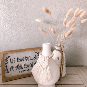 Pu&ograve; includere: Diffusore in ceramica bianca con un anello di legno e un fiocco di macram&egrave; bianco. Il diffusore &egrave; appoggiato su un tavolo di legno con un cartello che recita "We love because He first loved us 1 John 4:19". Dietro il diffusore ci sono erbe della pampa secche in un vaso bianco.