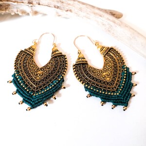 Puede incluir: Un par de pendientes de aro dorados con un diseño de borla verde. Los pendientes tienen un diseño detallado y ornamentado y son perfectos para agregar un toque de estilo bohemio a cualquier atuendo.