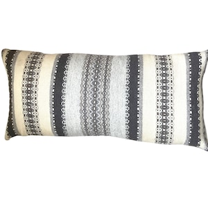 May include: A long rectangular pillow with a striped pattern in shades of gray, white, and black. The stripes are woven with a textured design.