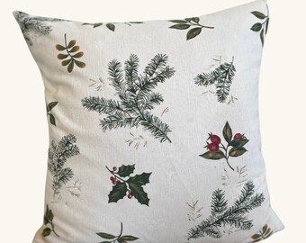 May include: A white throw pillow with a green and red floral pattern featuring pine branches, holly, and berries.