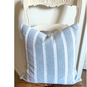 May include: A blue and white striped throw pillow with a woven texture. The pillow is sitting on a white chair with a carved back.