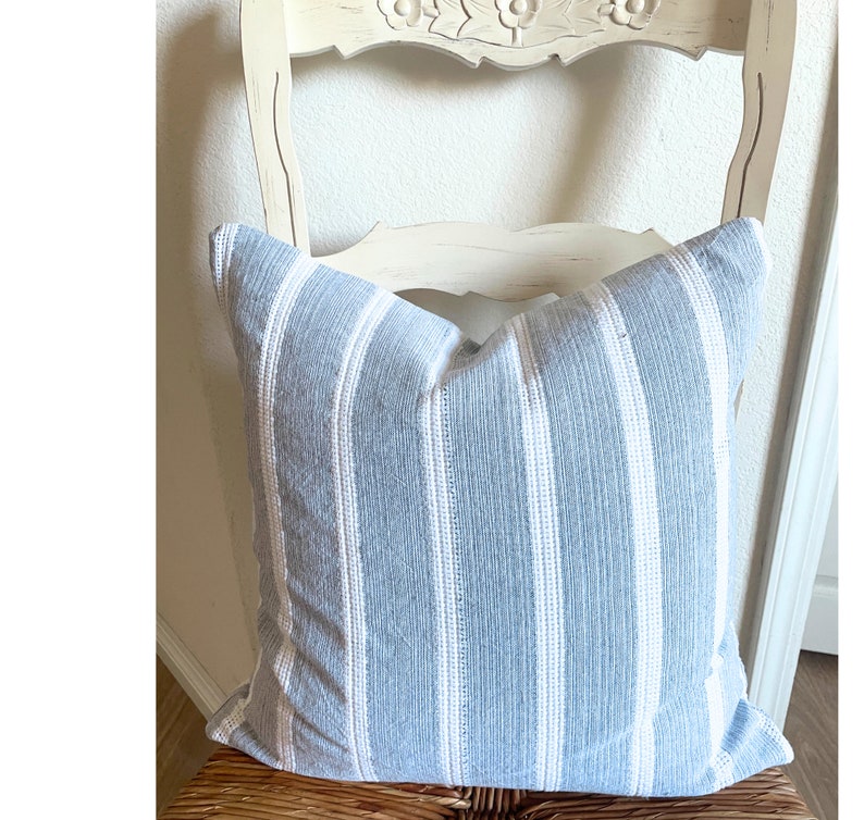 May include: A blue and white striped throw pillow with a woven texture. The pillow is sitting on a white chair with a carved back.