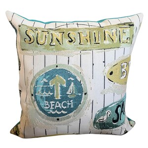 May include: Square decorative pillow with a beach theme. The pillow features the word "SUNSHINE" in a green banner, along with other beach-related signs. The pillow has a white background with vertical black lines and a teal border.