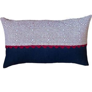 May include: Rectangular decorative pillow with a navy blue bottom, a red scalloped trim, and a top section with a white and burgundy geometric pattern. The pillow is designed for home decor and adds a touch of style to any room.