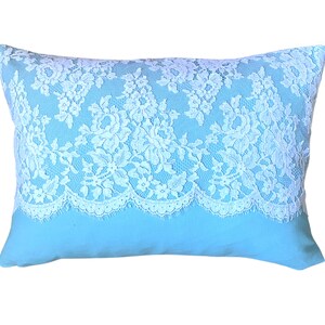May include: A light blue pillow with a white lace trim. The lace is a delicate floral pattern.