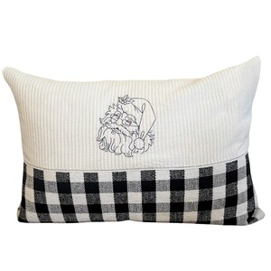 May include: A white and black checkered pillow with a white embroidered Santa Claus face on the top half.