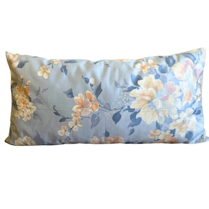 May include: A rectangular throw pillow featuring a light blue background with a repeating floral pattern. The design includes clusters of soft yellow, peach, and muted dark blue flowers with green leaves scattered across the fabric surface.