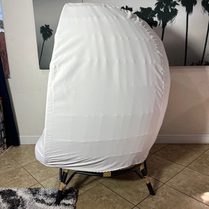 May include: A white chair cover with a woven rattan base and black legs. The chair is in a room with tiled floors and a rug.