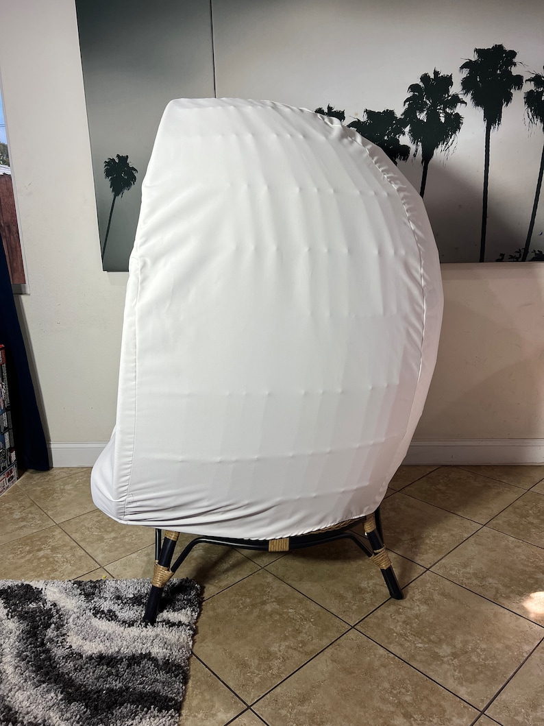 May include: A white chair cover with a woven rattan base and black legs. The chair is in a room with tiled floors and a rug.